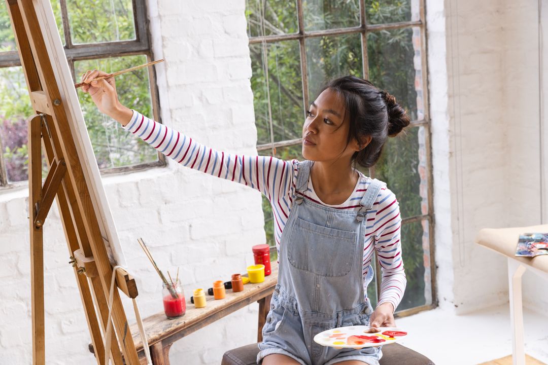 Young Asian Artist Painting on Canvas in Sunlit Studio