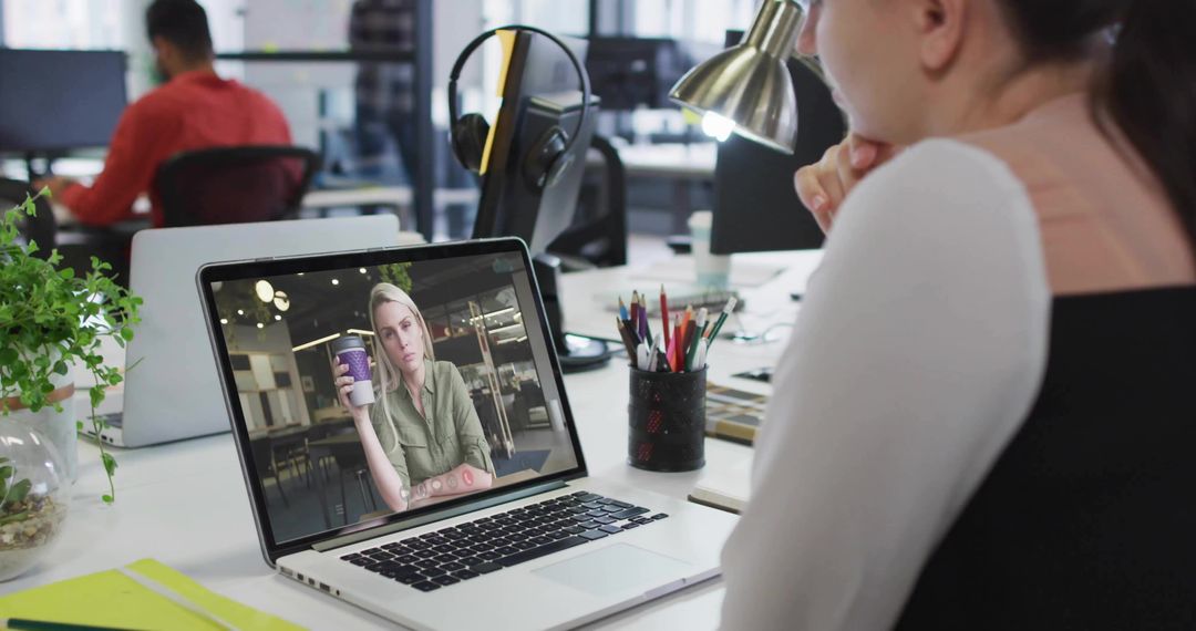 Remote coffee chat on laptop in modern open-plan office showing coworker video call