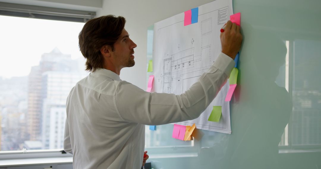 Executive Strategizing on Glass Board with Sticky Notes in Modern Office
