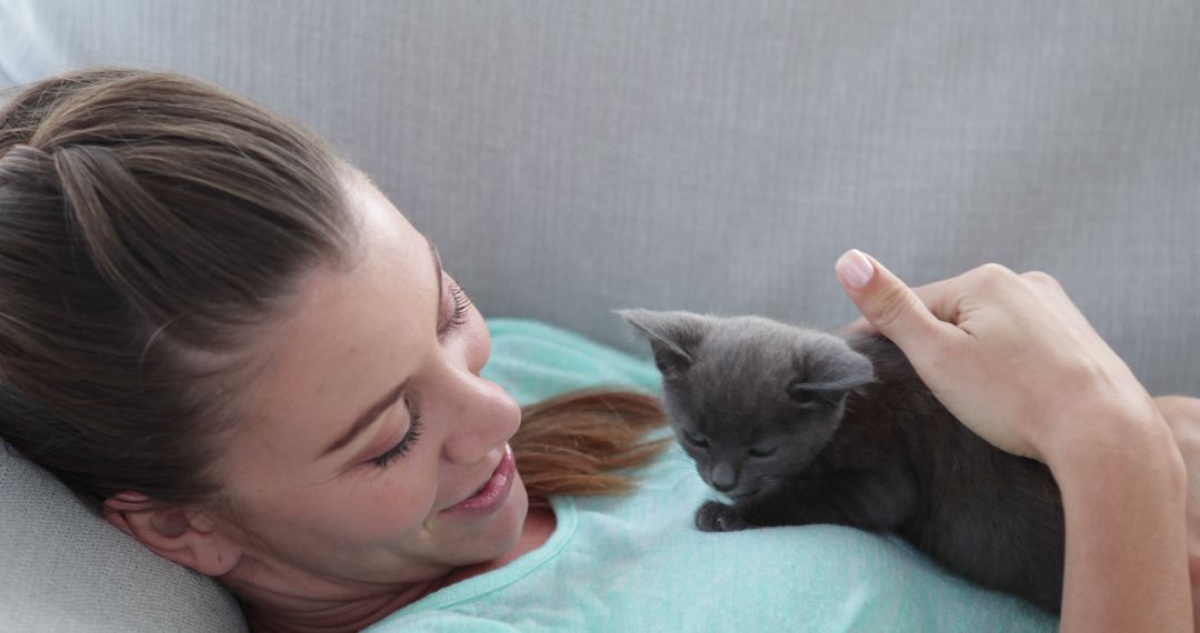 Woman relaxing on couch cuddling playful kitten