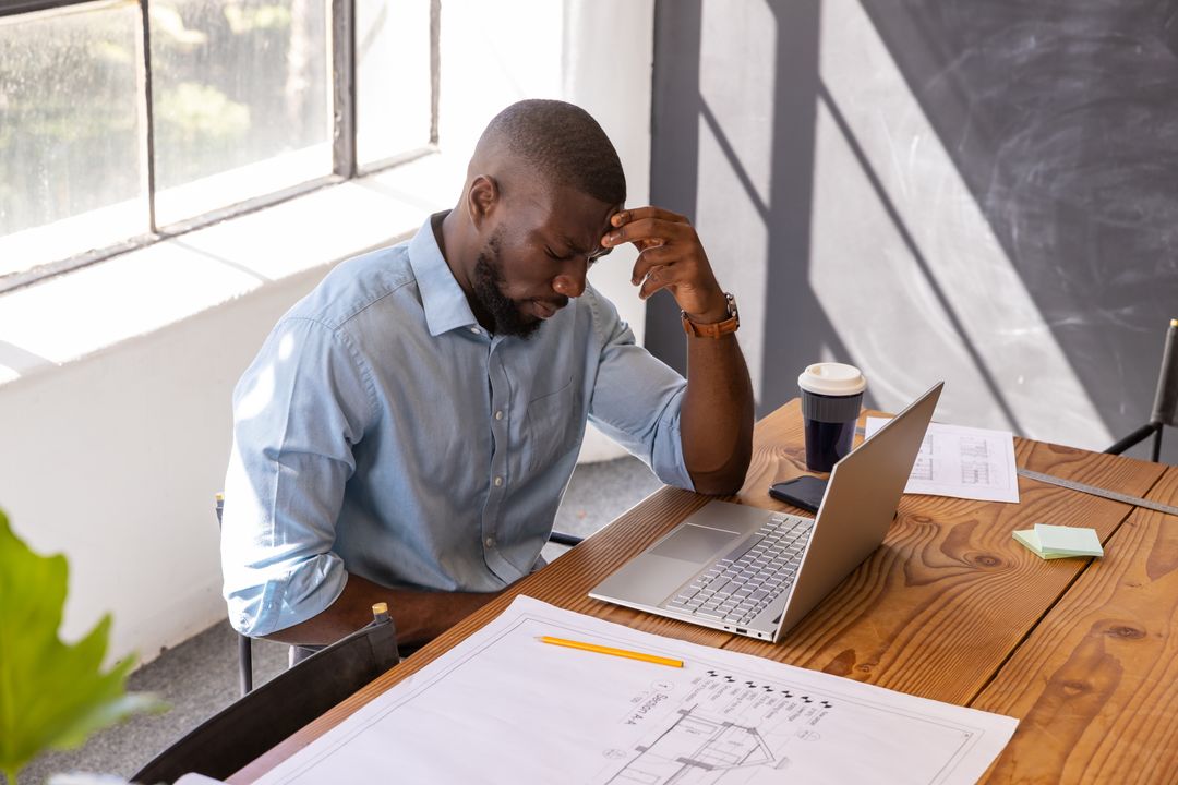 Architect Studying Blueprint with Laptop and Coffee at Office Desk