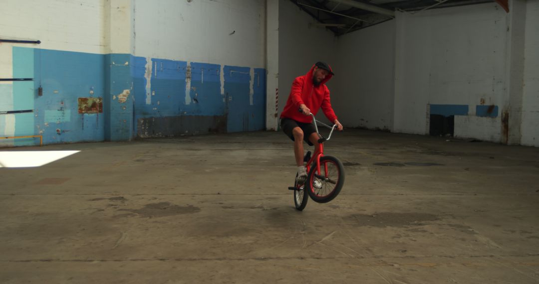 Man in Red Hoodie Performing Stunt on BMX Bike in Abandoned Warehouse - Free Images, Stock Photos and Pictures on Pikwizard.com