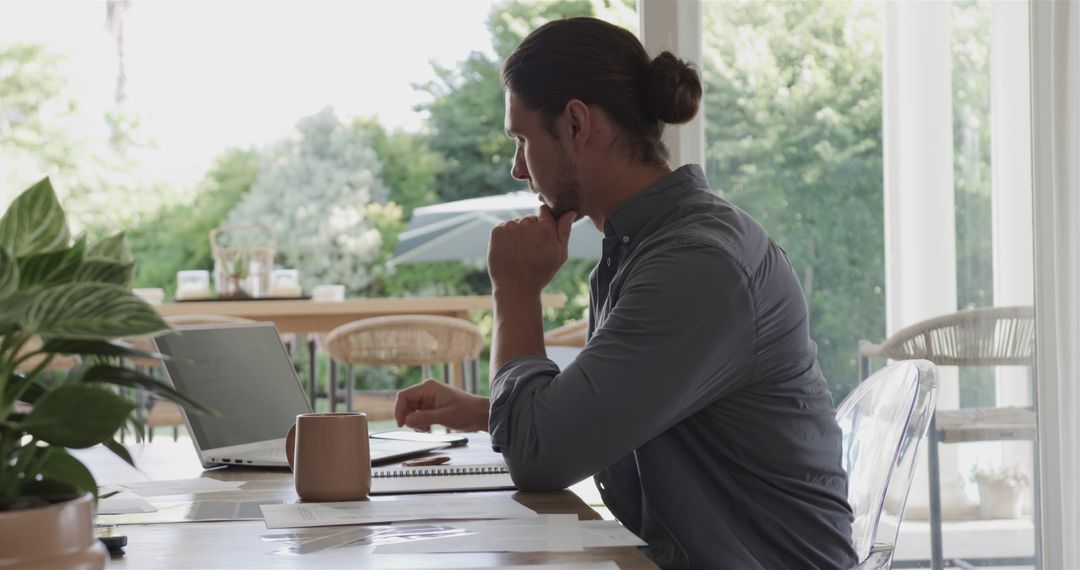 Man Focusing on Work at Home with Laptop and Notes Taking