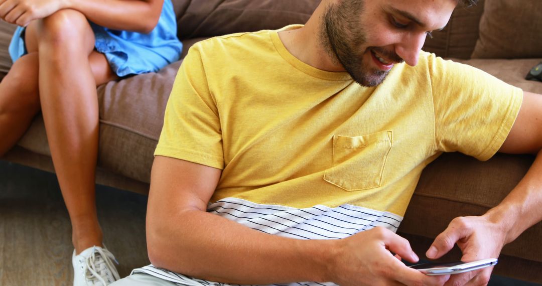 Man Texting and Smiling While Friend Sits on Couch - Free Images, Stock Photos and Pictures on Pikwizard.com