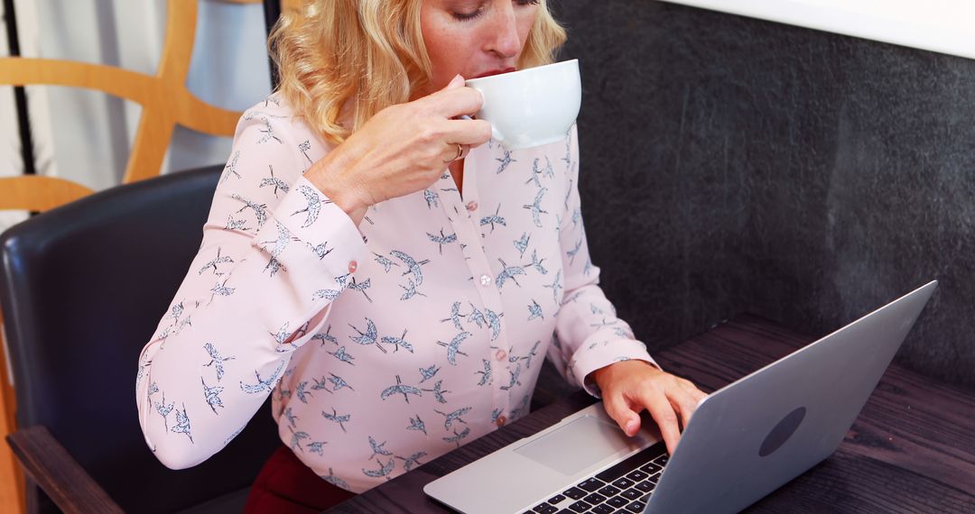 Blonde Woman Working on Laptop Drinking Coffee in Cafe - Free Images, Stock Photos and Pictures on Pikwizard.com