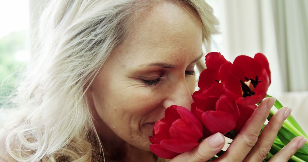 Mature Woman Enjoying the Fragrance of Red Tulips - Free Images, Stock Photos and Pictures on Pikwizard.com