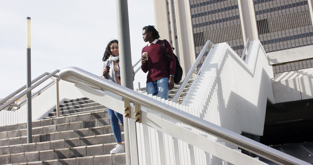 Diverse friends walking down urban zigzag staircase with coffee and smartphone commuting