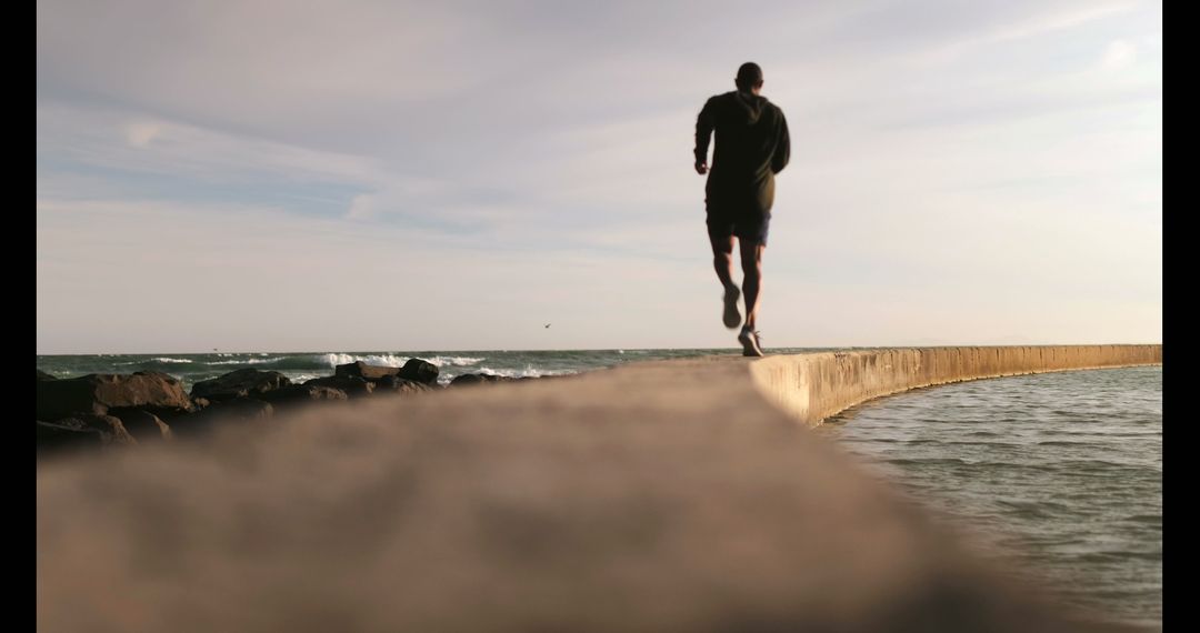 Man jogging on seawall by ocean during sunset