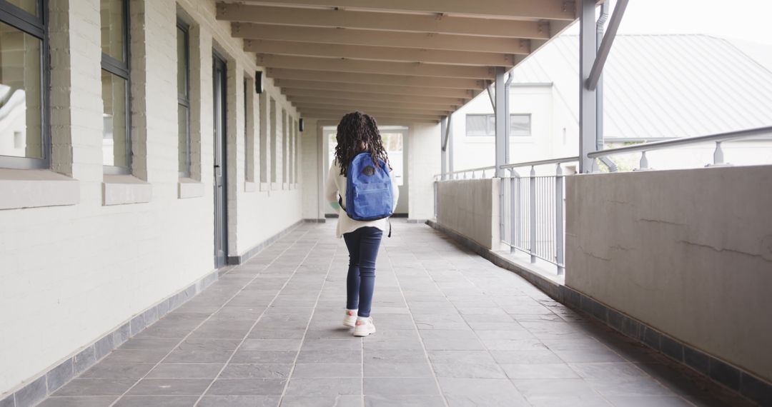 Young Student Walking in Empty School Corridor with Blue Backpack