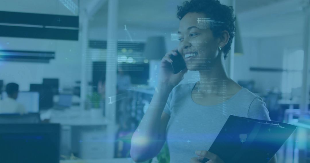 Smiling professional talking on phone while holding clipboard in modern office tech hub