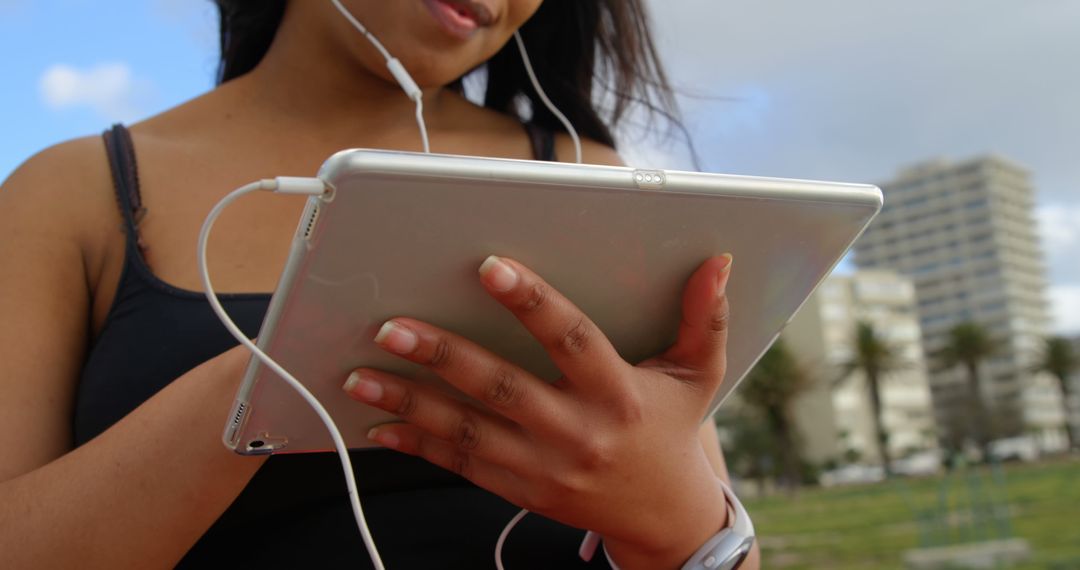 Woman Listening to Music While Holding Tablet Outside City Background - Free Images, Stock Photos and Pictures on Pikwizard.com