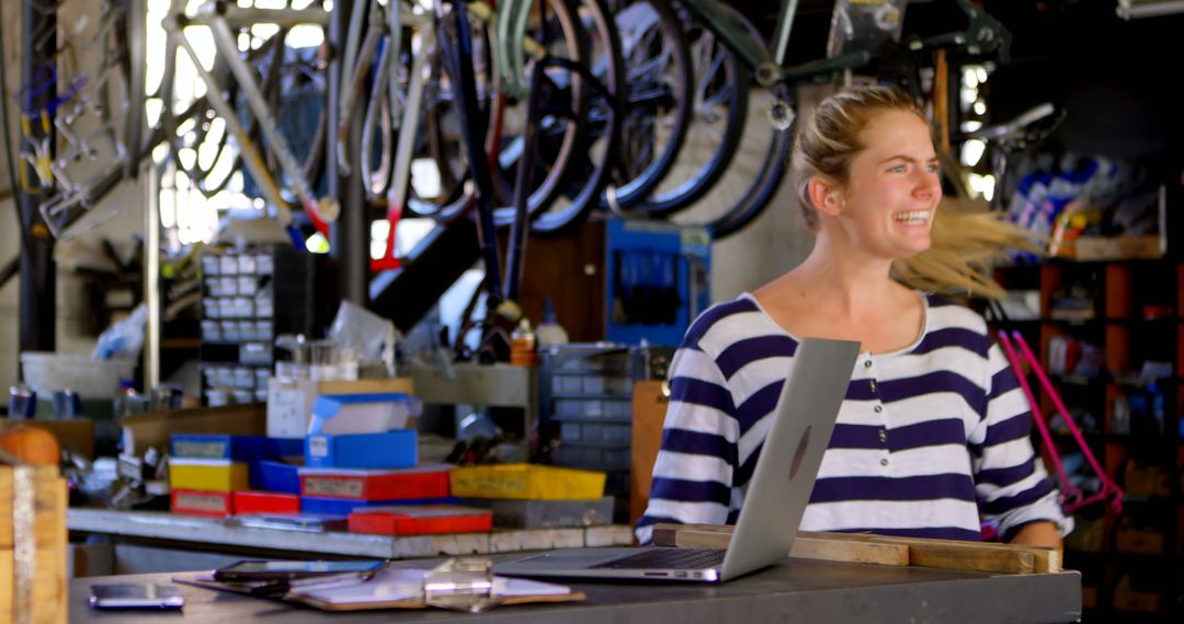 Smiling Woman Working on Laptop in Bicycle Repair Shop - Free Images, Stock Photos and Pictures on Pikwizard.com