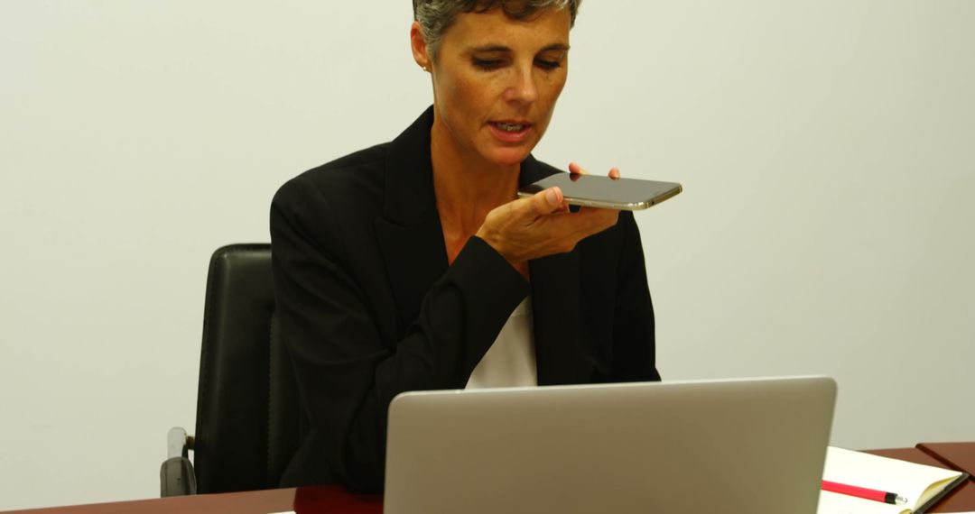 Businesswoman dictating to smartphone while working on laptop - Free Images, Stock Photos and Pictures on Pikwizard.com