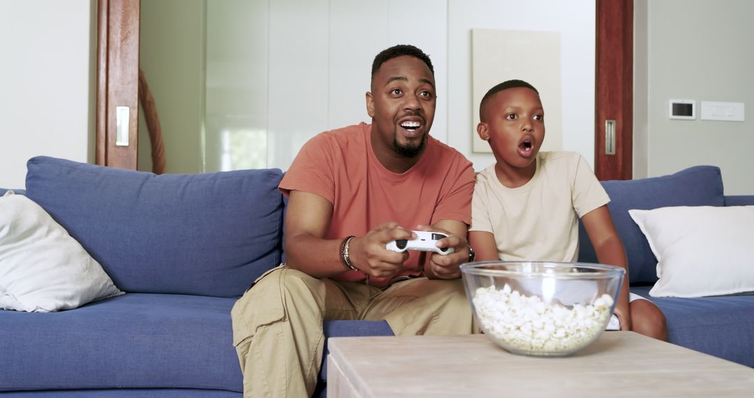 Father and Son Enjoying Video Game by Blue Couch with Popcorn