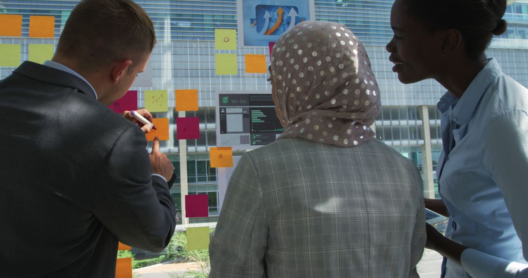 Diverse Team Collaborating Using Sticky Notes on Glass Wall