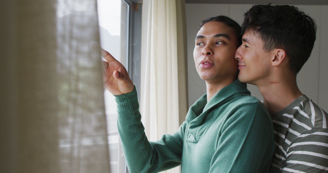 Happy Multiethnic Couple Embracing and Looking Through Window