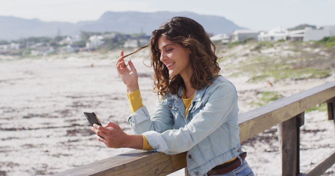 Smiling Woman Using Smartphone by Beachside Wooden Railing - Free Images, Stock Photos and Pictures on Pikwizard.com