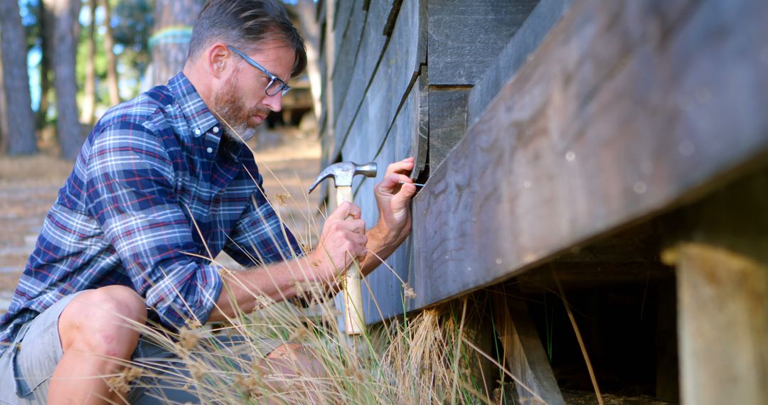 Man repairing wooden cabin with hammer outdoors on sunny day - Free Images, Stock Photos and Pictures on Pikwizard.com