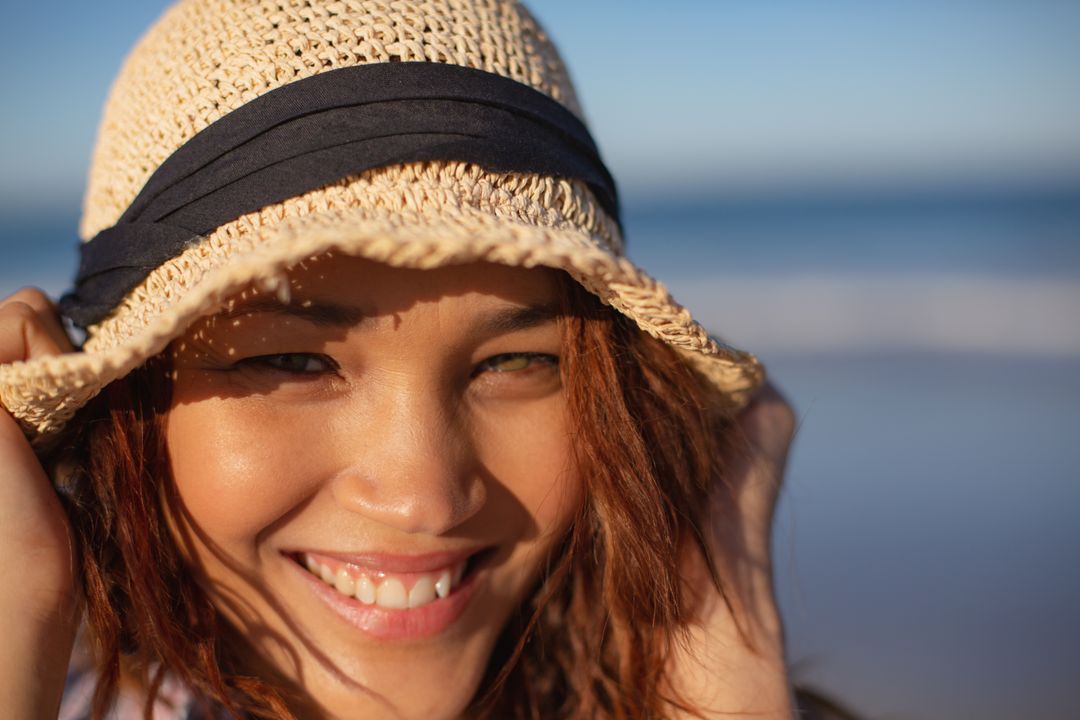 Smiling Biracial Woman Wearing Hat on Sunny Beach - Free Images, Stock Photos and Pictures on Pikwizard.com