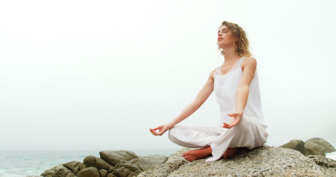Caucasian Woman Meditating in Yoga Pose by Sea Outdoors