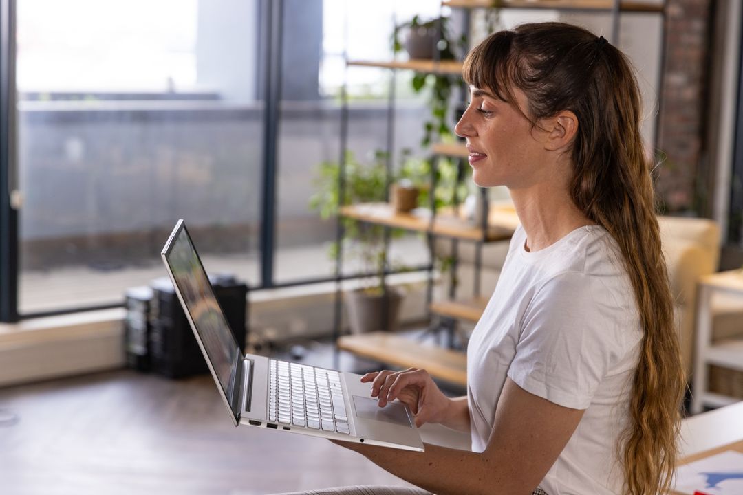 Young Woman Smiling While Using Laptop in Bright Modern Office