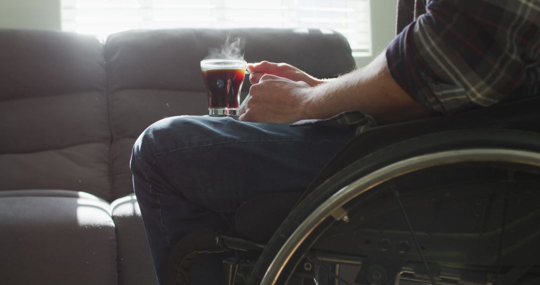 Person in wheelchair holding coffee in cozy home interior - Free Images, Stock Photos and Pictures on Pikwizard.com