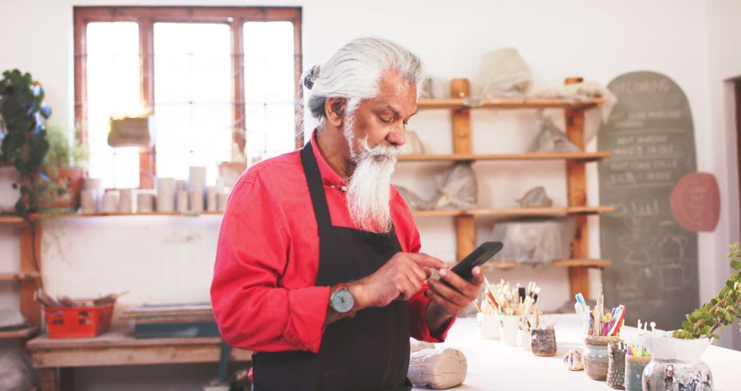 Senior Artisan Texting on Smartphone in Ceramics Studio - Free Images, Stock Photos and Pictures on Pikwizard.com