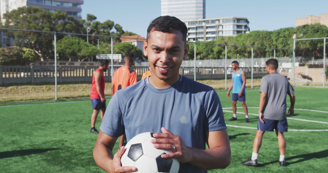 Portrait of biracial male football player looking at camera and holding ball on outdoor pitch - Free Images, Stock Photos and Pictures on Pikwizard.com