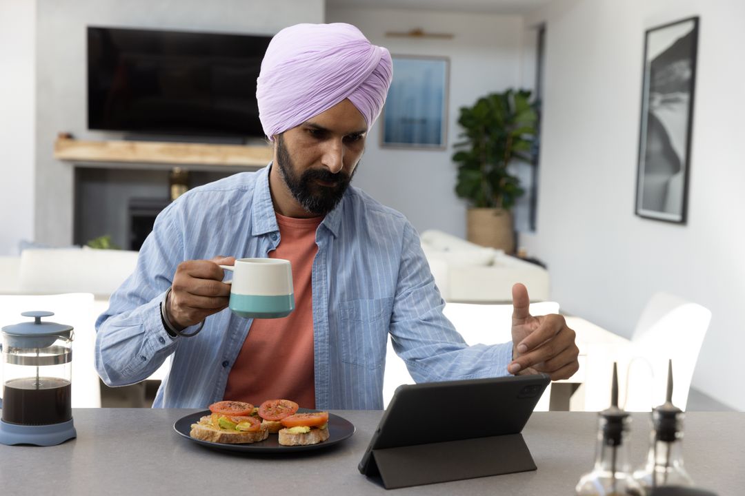 Man in Turban Enjoying Breakfast While Working on Tablet at Home