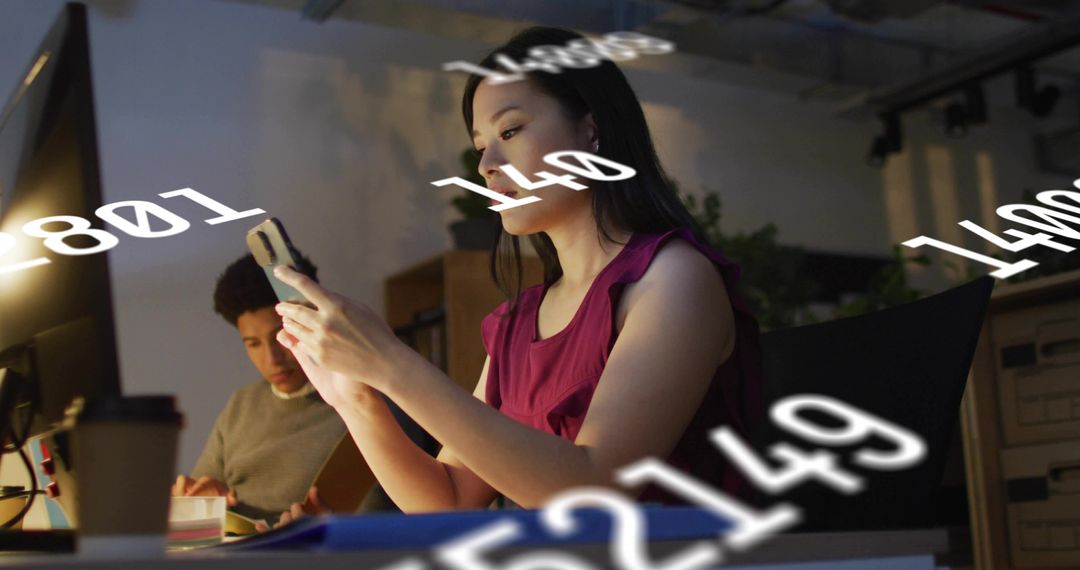 Woman checking smartphone at office desk with floating numeric data overlay