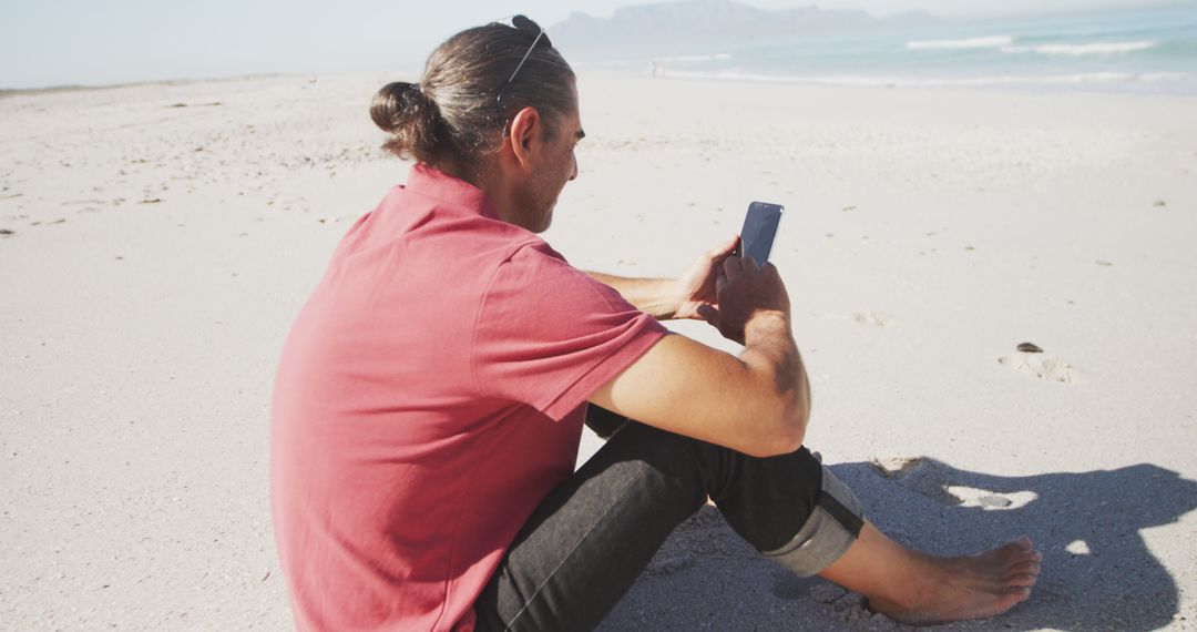 Man relaxing on beach watching smartphone during sunny day - Free Images, Stock Photos and Pictures on Pikwizard.com