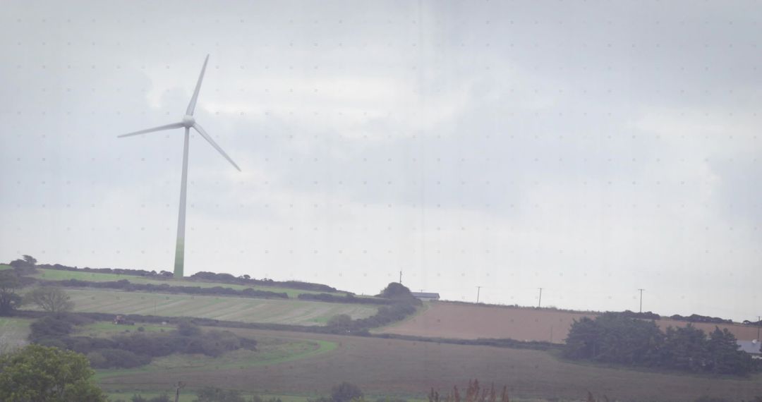 Single wind turbine standing on rural ridge overlooking rolling farmland under cloudy sky