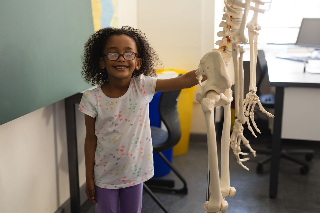 Happy black schoolgirl holds skeleton model in classroom. - Free Images, Stock Photos and Pictures on Pikwizard.com