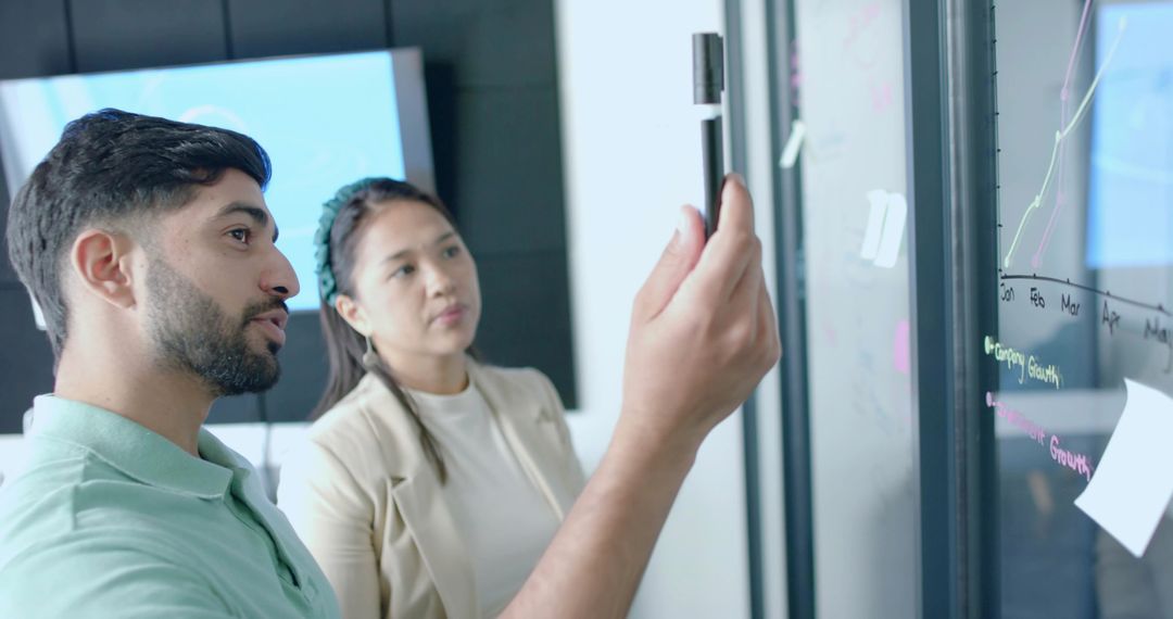 Coworkers Analyzing Data on Glass Board in Modern Office