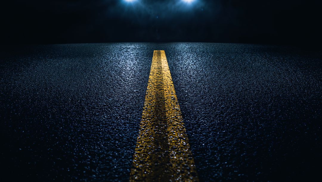 Double Yellow Line Reflecting on Wet Asphalt at Night with Headlights Casting Glow