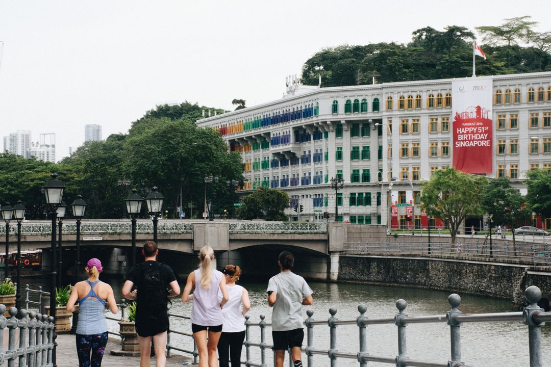 Group of Friends Jogging Along Riverside Path, Historic Building in Background