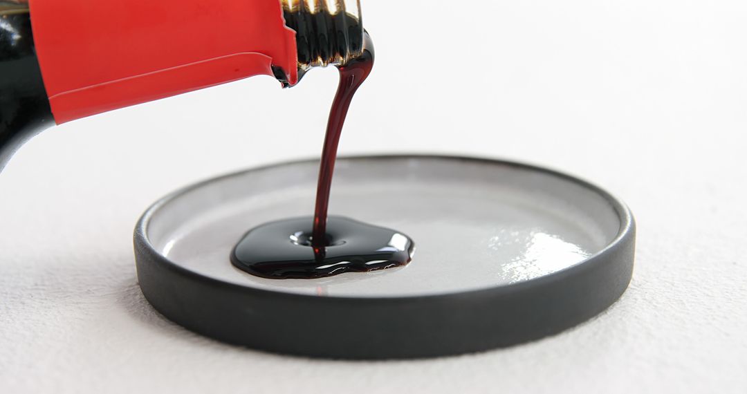 Thick Dark Liquid Pouring from Red Bottle into Dish