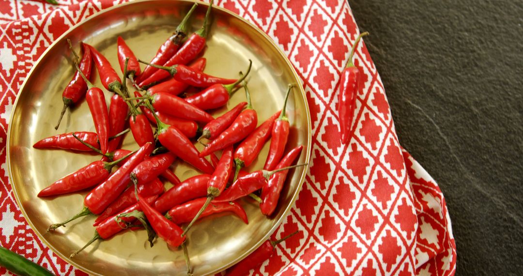 A brass plate with red chilies on patterned cloth adds spice to dishes and decor. - Free Images, Stock Photos and Pictures on Pikwizard.com
