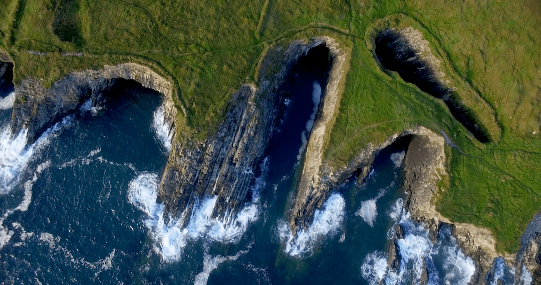 Transparent Waves Crash Against Rugged Green Cliff Coastline
