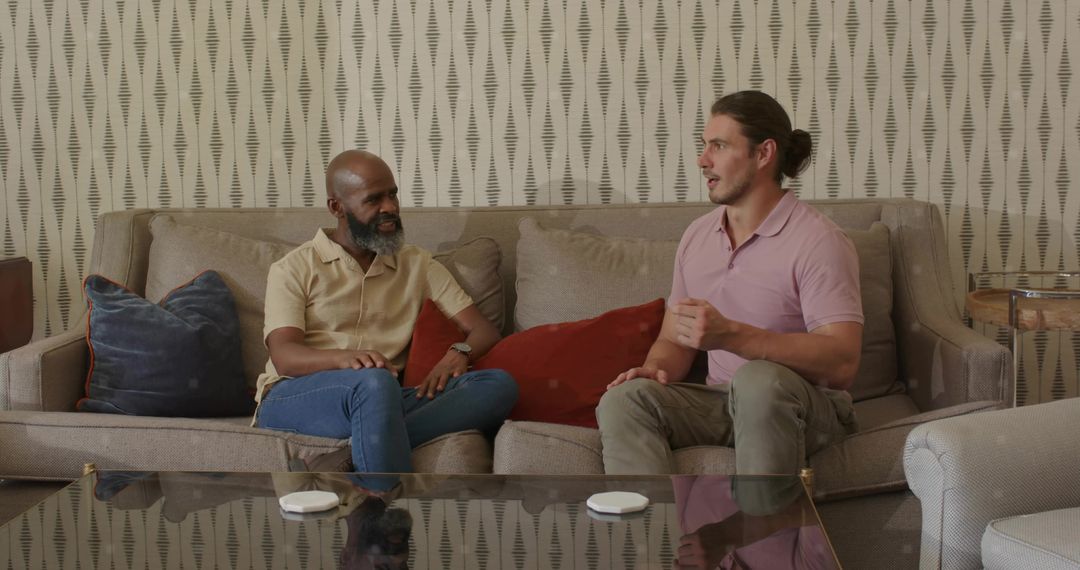 Two men chatting on sofa in stylish living room with patterned wallpaper and glass table