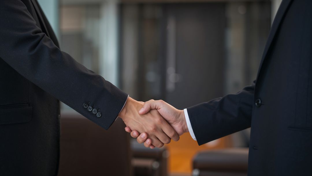 Shaking hands sealing corporate deal in modern office lobby showing suit cuffs