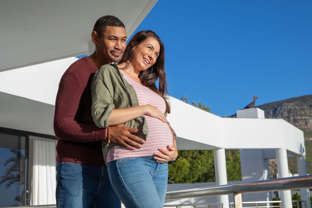 Expecting Couple Embracing On Sunny Terrace With Mountain View