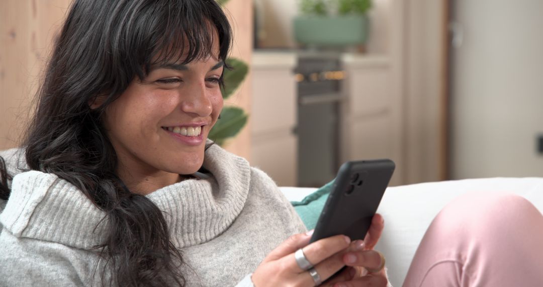 Woman Relaxing on Sofa Smiling at Smartphone in Comfortable Living Room