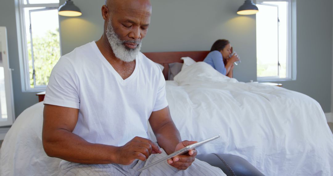 Mature man using tablet while woman relaxing on bed with coffee - Free Images, Stock Photos and Pictures on Pikwizard.com