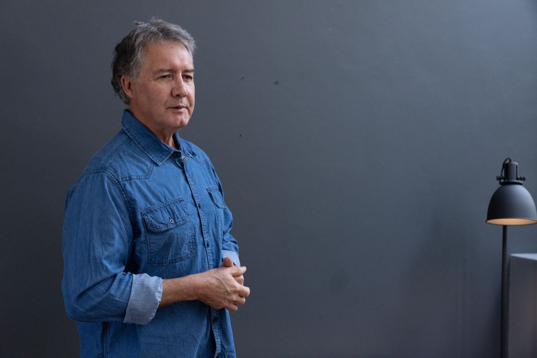 Senior Man in Denim Shirt Standing by Modern Black Desk Lamp