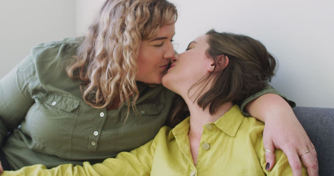 Caucasian lesbian couple kissing and sitting on couch - Free Images, Stock Photos and Pictures on Pikwizard.com