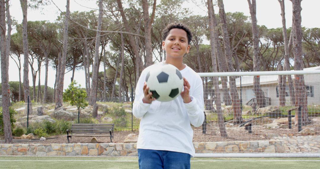 Smiling Boy Holding Soccer Ball on Outdoor Field Before Goal