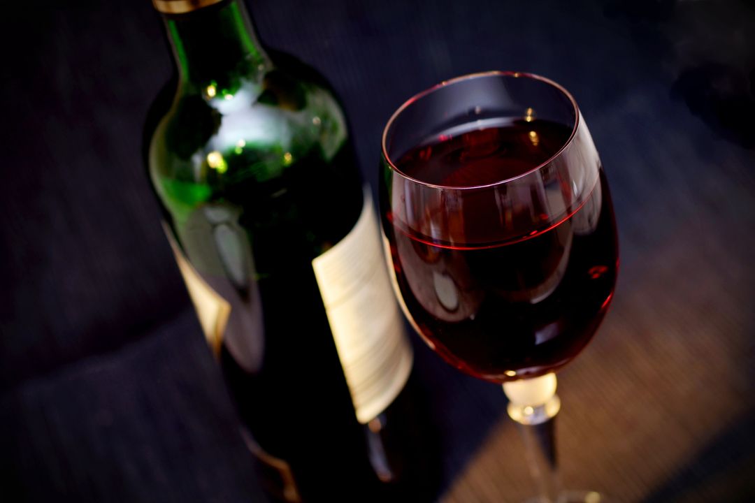 Rich Red Wine in Crystal Glass Featuring Blurred Bottle on Dark Elegant Backdrop