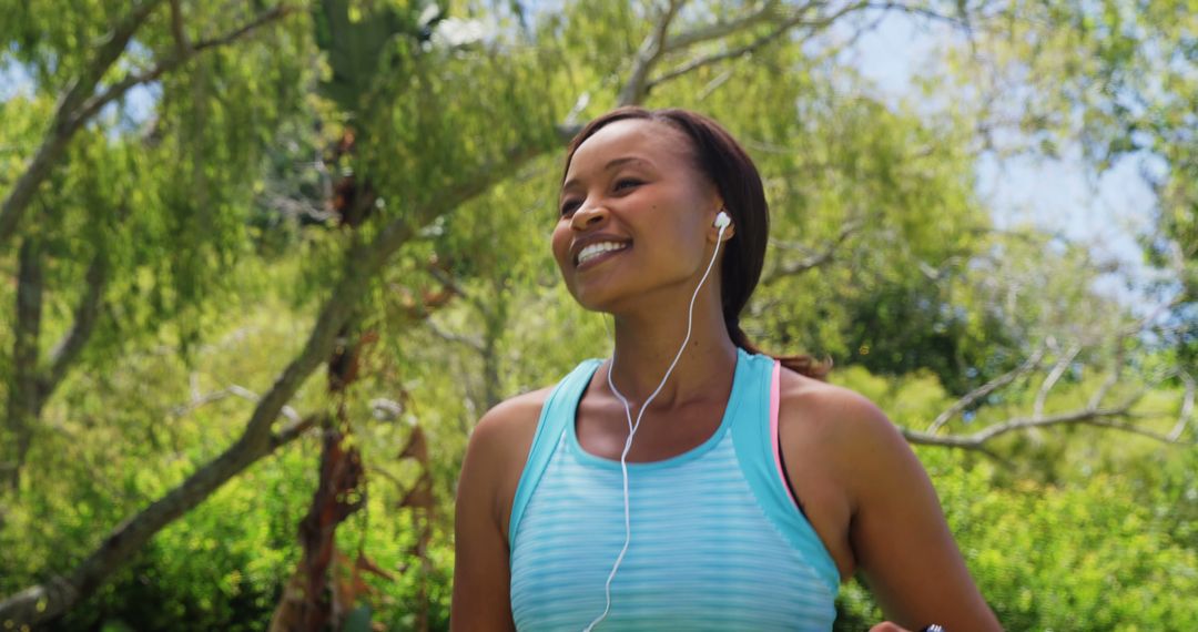 Smiling Woman Jogging Outdoors with Earbuds in Park - Free Images, Stock Photos and Pictures on Pikwizard.com