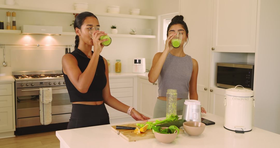 Two Friends Enjoying Fresh Green Smoothies in Modern Kitchen
